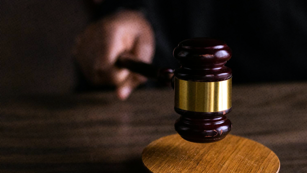 A close up of a judge's hand holding a gavel with a gold band.