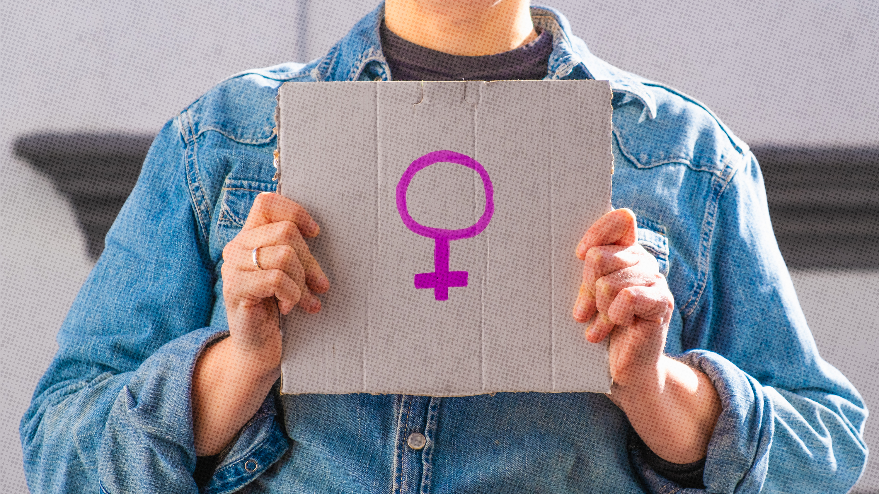 Woman wearing a jean jacket holding a sign outdoors showing the female symbol.