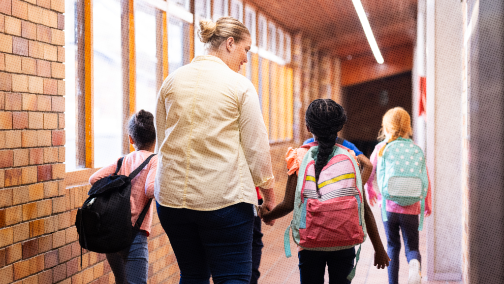 A white female teacher in a yellow shirt walking down a school hallway with a 6 year old black female student with a backpack.